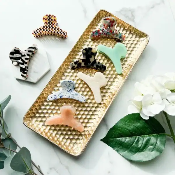 A variety of colorful hair claw clips arranged on a decorative tray, with greenery and a white flower in the background. Sold as a set perfect for a Mothers Day Gift Basket 