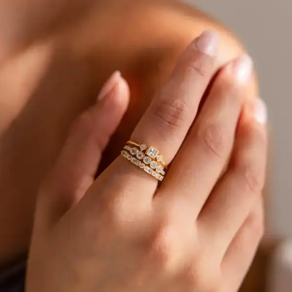 A close-up of a hand displaying multiple stacking rings with diamonds on a background of a soft, neutral color.