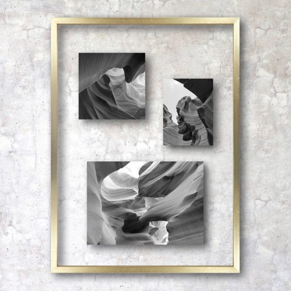 Three black and white photographs of abstract rock formations mounted in a gold frame against a textured wall.