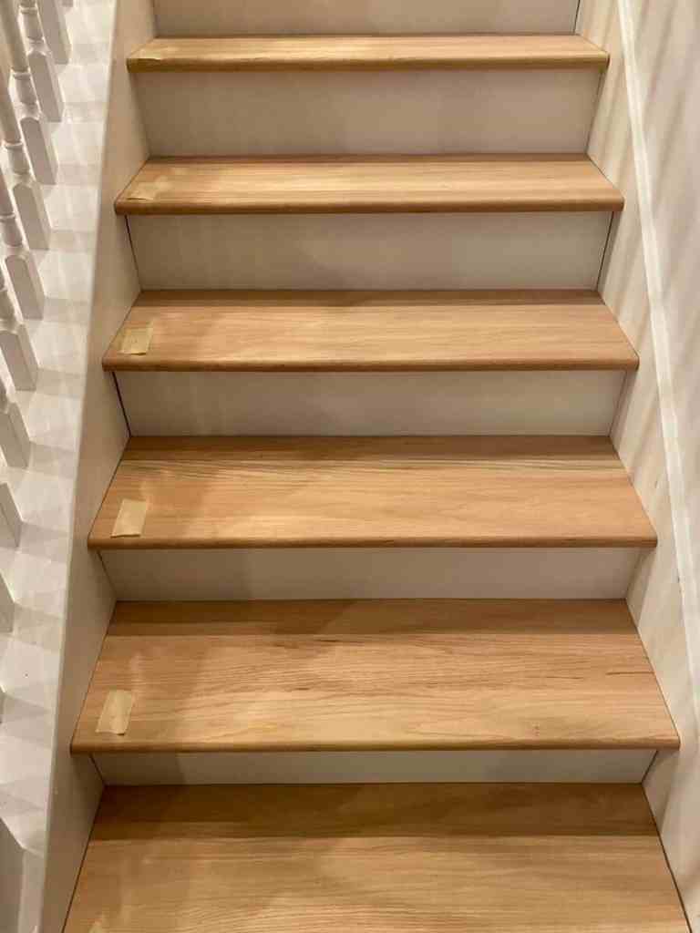 Wooden stairs with a light finish, featuring tape on each step, leading upwards.