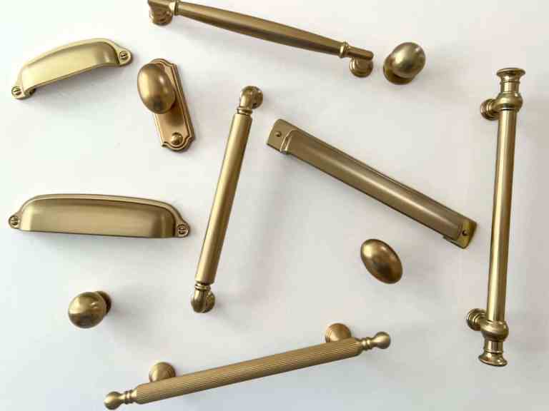 Various brass round and egg shaped knobs, bar pulls, cup pulls, handles arranged on a white background.