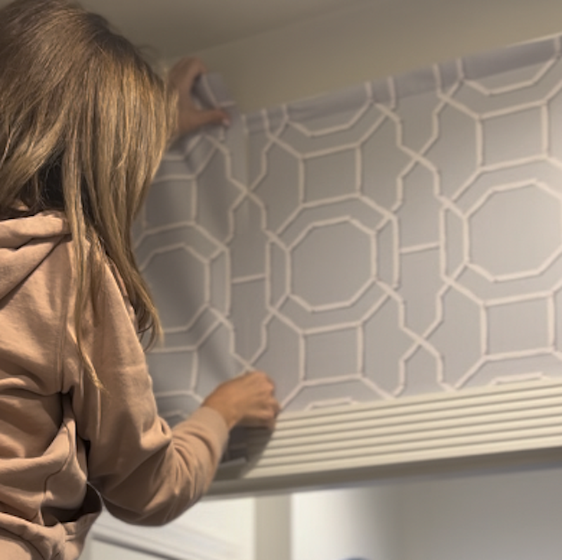 A person installing a patterned window treatment, featuring a geometric design, in a home setting.