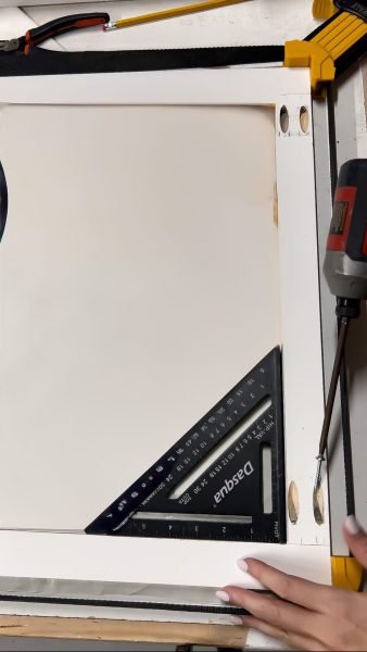 Close-up of a wooden frame under construction for a wall-mounted drying rack, featuring a square tool and drill, with visible pocket holes.
