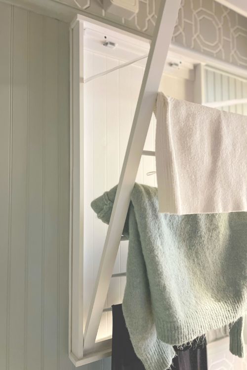 Hanging clothing on a wooden drying rack in a softly lit room with patterned wallpaper.