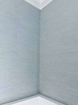 Blue grasscloth wallpaper in a corner of a white wall, with trim installed 3/4 up the wall, ready for paint to be applied. This image showcases the process of wallpaper and matching paint for a cohesive, stylish room design.