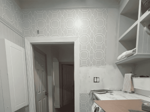 An unfinished kitchen area showcasing a patterned light blue wall, an open doorway leading to another room, and a countertop with kitchen appliances.