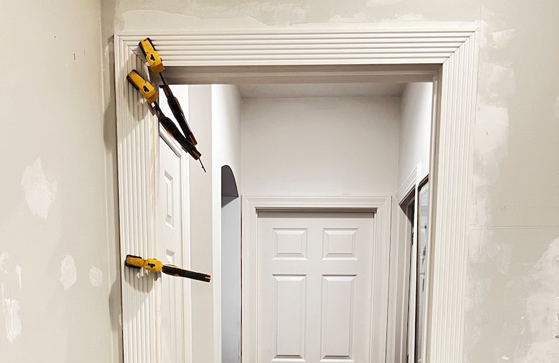 A doorway framed with decorative molding, featuring clamps securing the trim in place during installation. 
