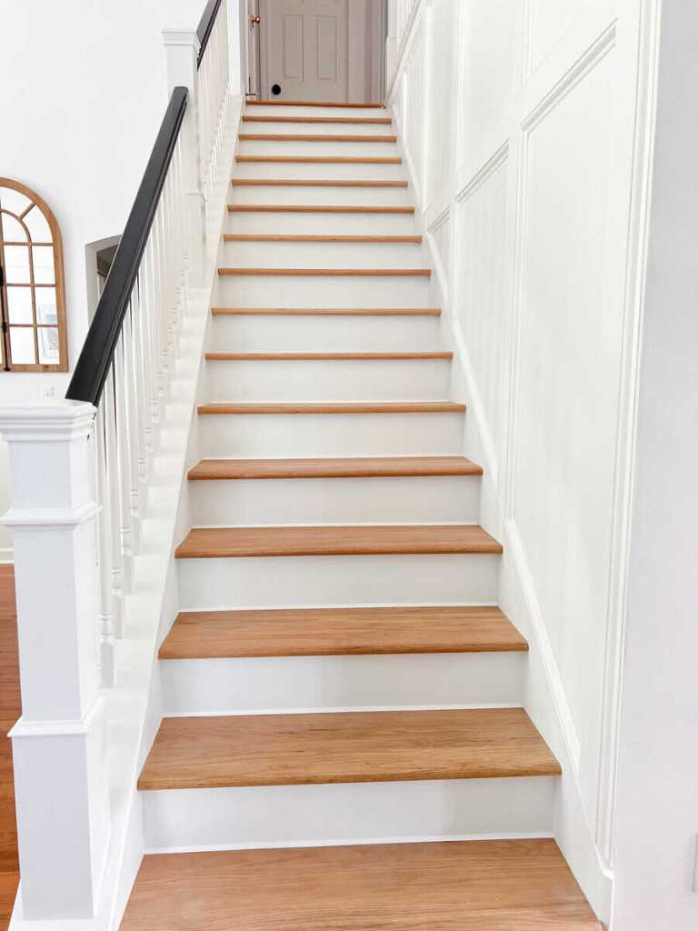 A view of a staircase with light wooden steps and white walls, leading to an upper level, featuring a black handrail and a door at the top.