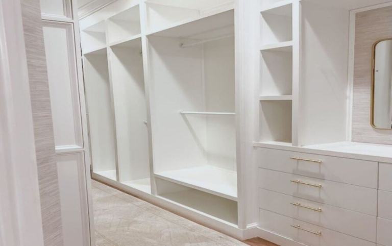 Empty custom walk-in closet with built-in shelving, dresser, and vanity wall after renovation
