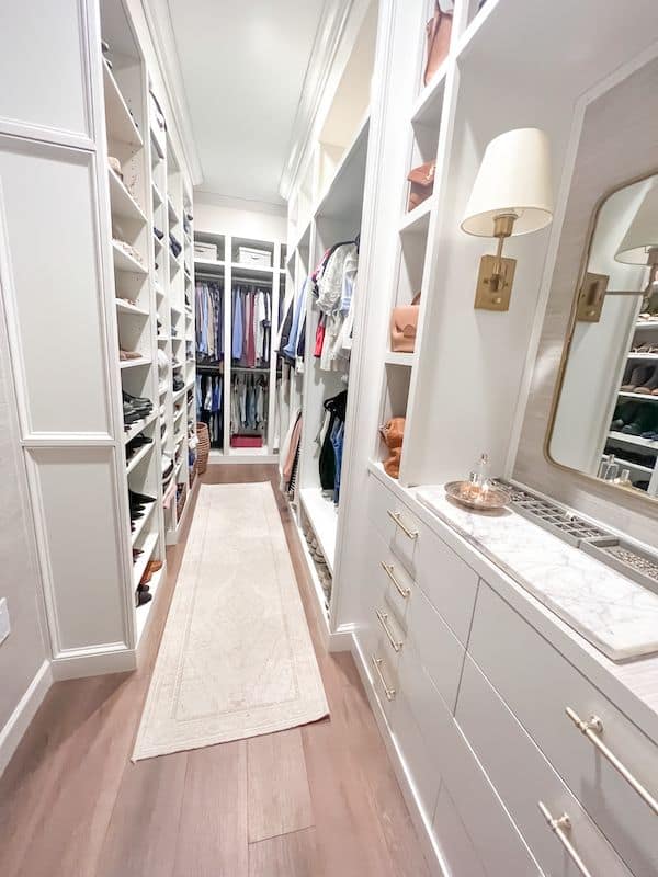 After photo of a  renovated narrow primary walk-in closet with a built-in dresser, frames for hanging space, built in bookcase for folded items and updated lighting. 