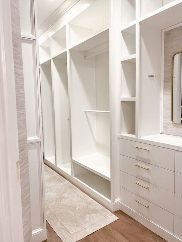 After photo of an empyy recently renovated narrow primary walk-in closet with a built-in dresser and frames for hanging space