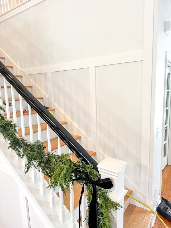 A staircase with wooden steps and a black railing decorated with greenery and a black bow.