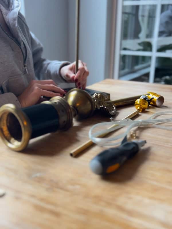 A person assembling decorative lamp parts on a wooden table, with various components and tools visible.