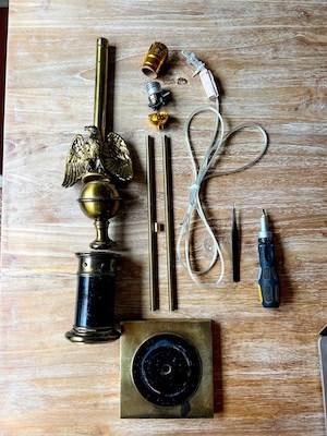 Vintage table lamp being rewired, with tools and materials like wire cutters, a screwdriver, and a new lamp cord laid out on a work surface.