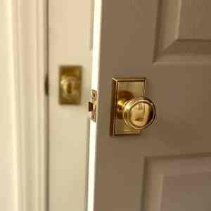 Close-up of a white door with a brass doorknob and lockset, partially open.