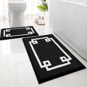 Black and white geometric bathroom rugs placed in front of a toilet and bathtub on a tiled floor.