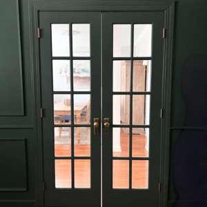 French doors painted dark green to match a color-drenched home office, with brass hardware and white hallway beyond.