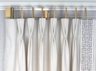 Close-up view of white curtains with a decorative black and white geometric trim, featuring gold curtain hooks for an elegant look.