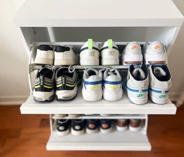 Shoe rack displaying various pairs of sneakers, including Nike and other brands, arranged neatly on white shelves.