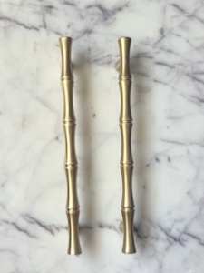 Two gold-colored bamboo-style drawer handles on a marble surface.
