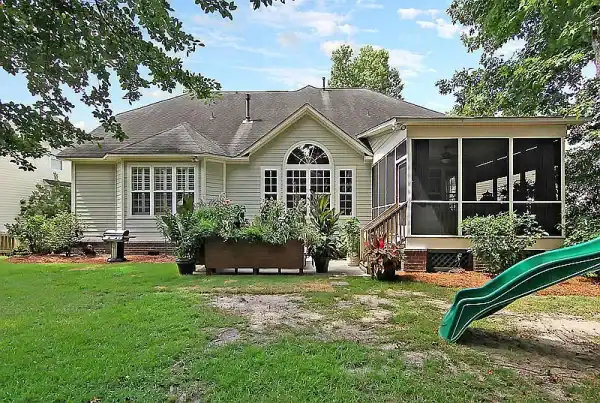 Rear view of a house surrounded by a well-maintained backyard, featuring a variety of plants and a children's slide.