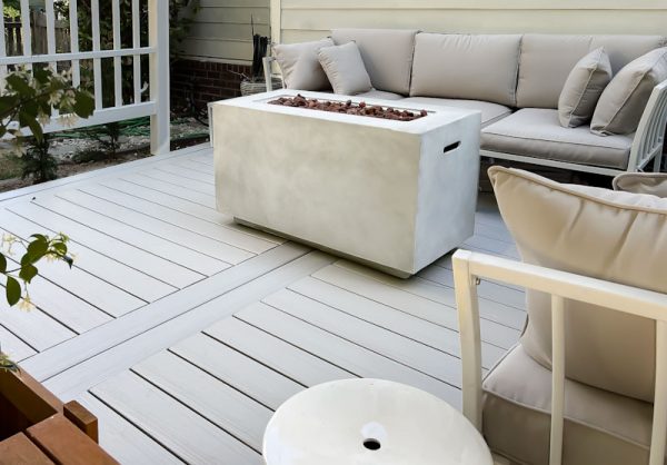 Cozy outdoor living space featuring a modern sectional sofa, a concrete fire table, and light hardwood decking.