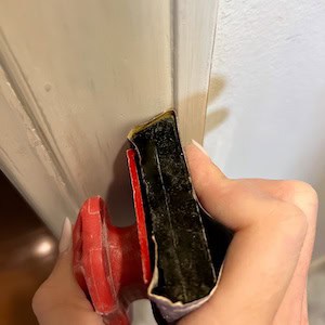 A close-up of a hand holding a painting tool against a wall, with the focus on the tool and its alignment with the edge of the door frame.