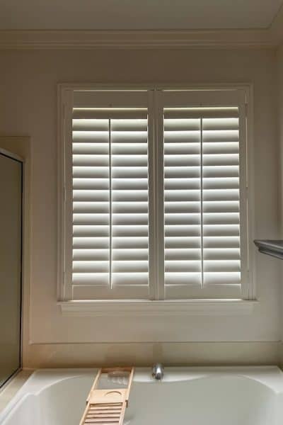 Before privacy film for bathroom window. A bathroom window with plantation shutters, allowing soft natural light to filter through while maintaining privacy.