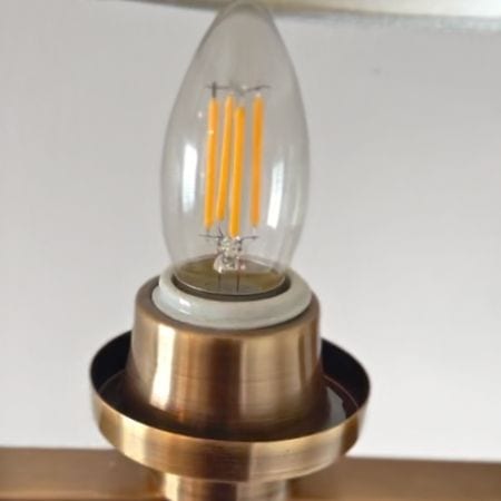 Close-up of a vintage-style light bulb with a flame shape, featuring exposed filaments, mounted on a brass fixture.