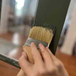 A hand holding a paintbrush applying green paint to a interior French door