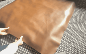 Close-up of hands holding a piece of faux leather fabric on a textured surface, ready for a DIY project.