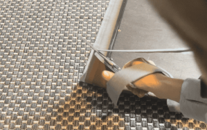 Person using scissors to cut a strip of foam or fabric while working on a DIY project on a textured floor.