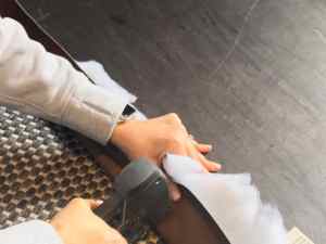 A person using a staple gun to attach batting to faux leather fabric while creating a DIY headboard.