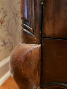 Close-up view of the carved edge of a wooden piece of furniture, showcasing its detailed craftsmanship and a small imperfection on the surface.
