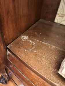 Close-up of a wooden shelf showing a white circular ring stain on the surface, indicating a mark left by a cup or glass.