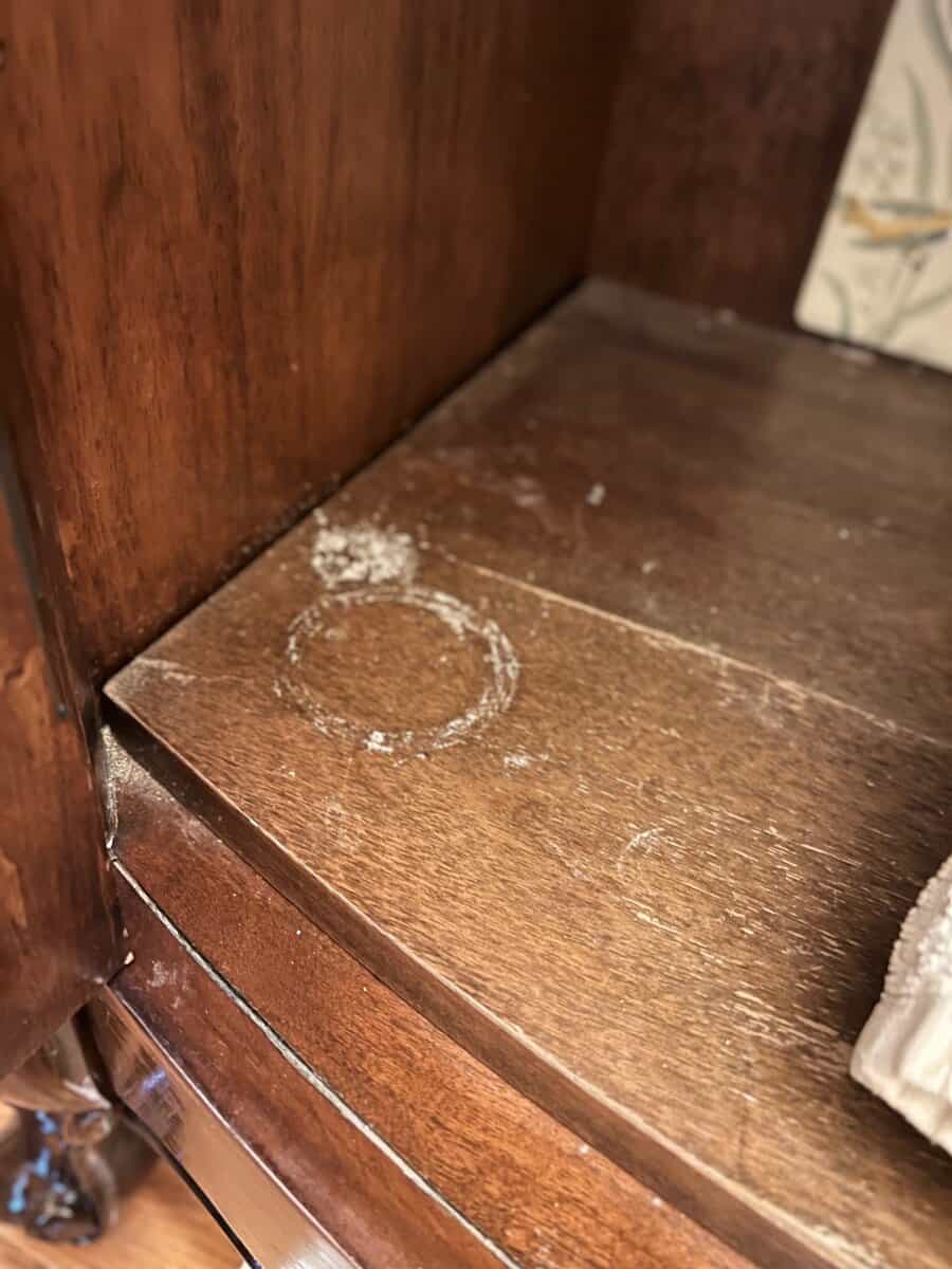 Close-up of a wooden shelf showing a white circular ring stain on the surface, indicating a mark left by a cup or glass.