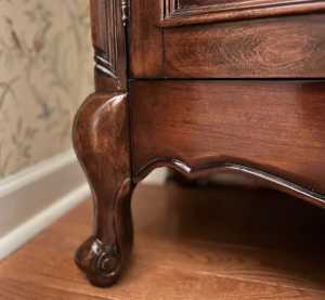 Close-up of the ornate wooden leg of a vintage furniture piece with a polished finish.
