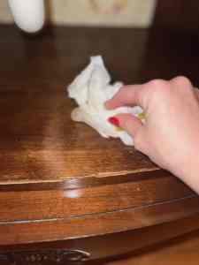A hand with red nail polish is cleaning a wooden tabletop with a cloth.