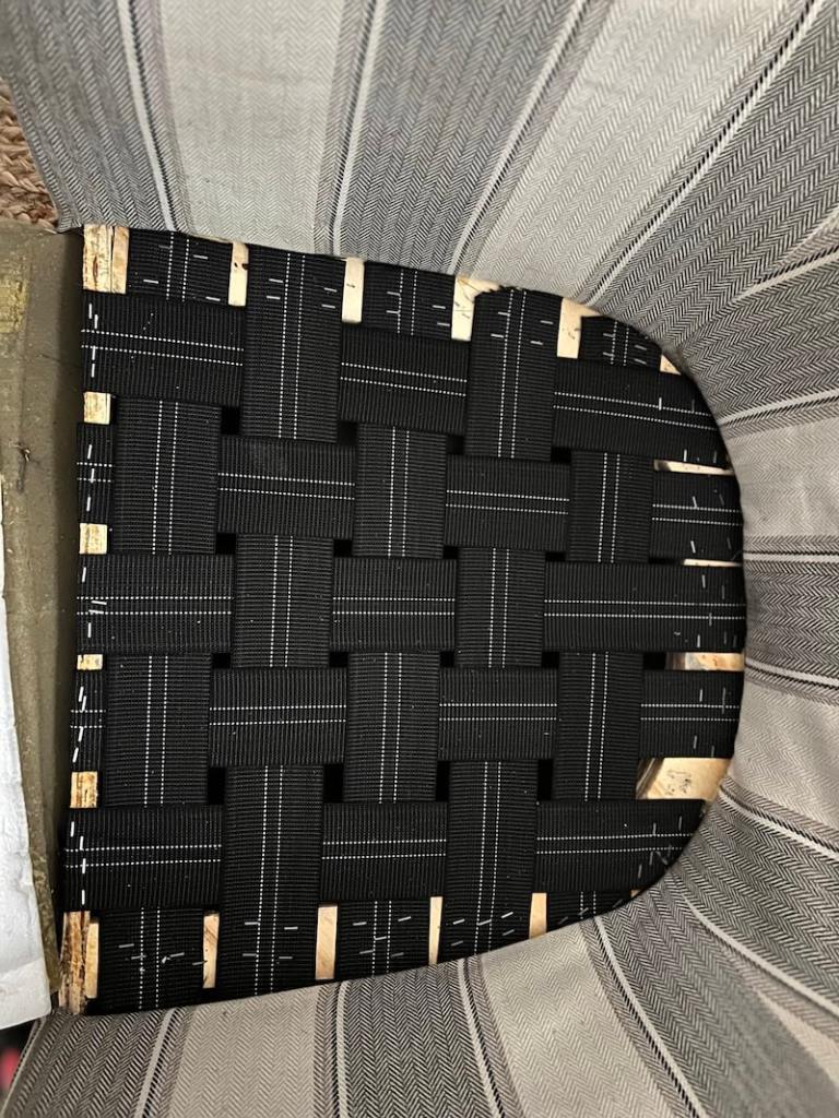 Close-up view of a woven chair seat made of black fabric straps and wooden supports.