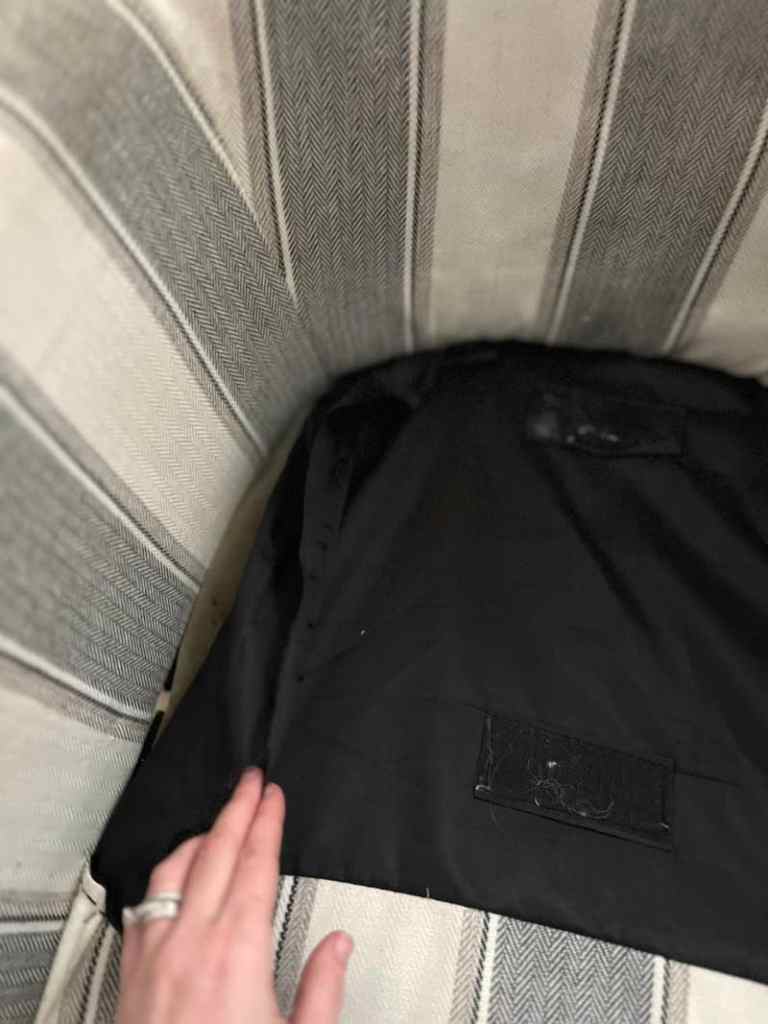 Close-up of a hand resting on a black fabric with tags at the bottom of a striped upholstery.