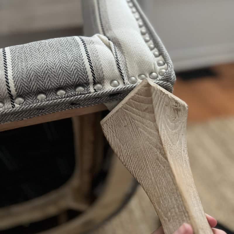 Close-up of a wooden tool being used to adjust or repair the fabric on a chair with decorative nailhead trim.