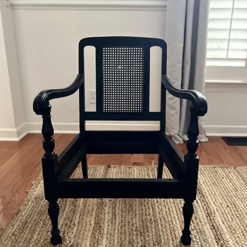 A black wooden chair with a cane backrest, featuring carved arms and legs, placed on a woven area rug.