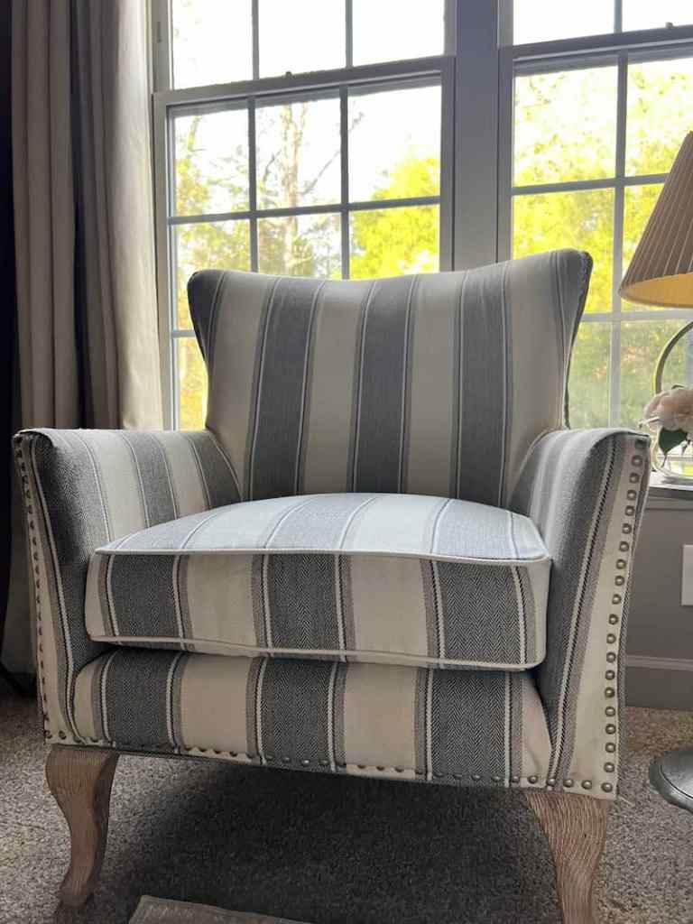 A cozy armchair with a striped fabric design, featuring a high back and cushioned seat, positioned near large windows with natural light.