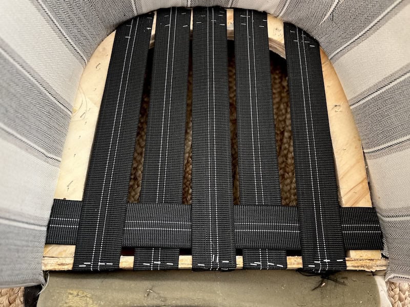 Top view of a chair seat showing black woven fabric straps arranged in a crisscross pattern over a wooden base.