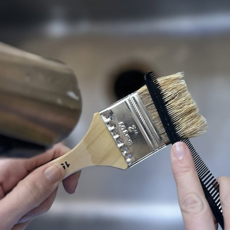using a hair comb to clean a paint brush