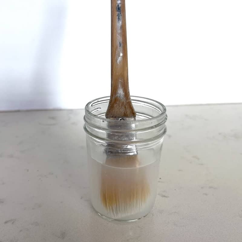 A wooden brush standing upright in a glass jar filled with rubbing alcohol 
