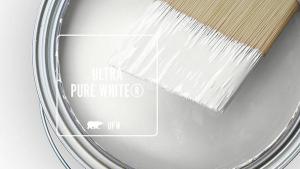 Close-up of a paint can with a paintbrush dipped in white paint, featuring 'ULTRA PURE WHITE' by behr.