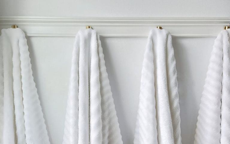 Bathroom towel rack made with wood trim and gold hooks holding multiple bath towels
