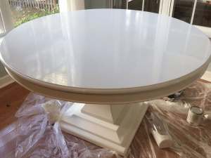 A freshly painted glossy white round table with a sturdy pedestal base, after filling grooves and repainting the surface