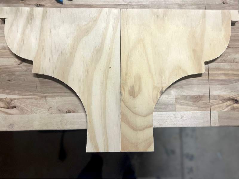 Two matching decorative shelf brackets cut from wood and ready for sanding
